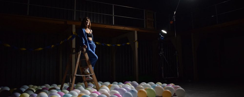 Judith sits on a ladder in blue suit, surrounded by balloons